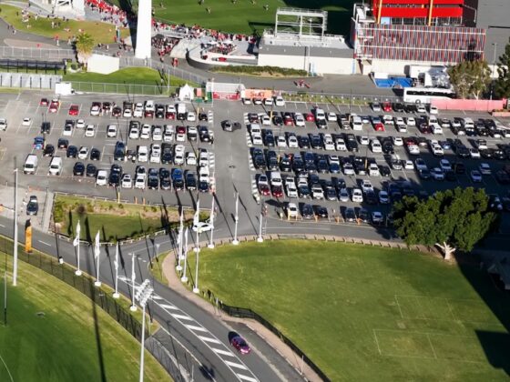 Aerial view of crowded parking lot adjacent to sports stadium with green field and spectators